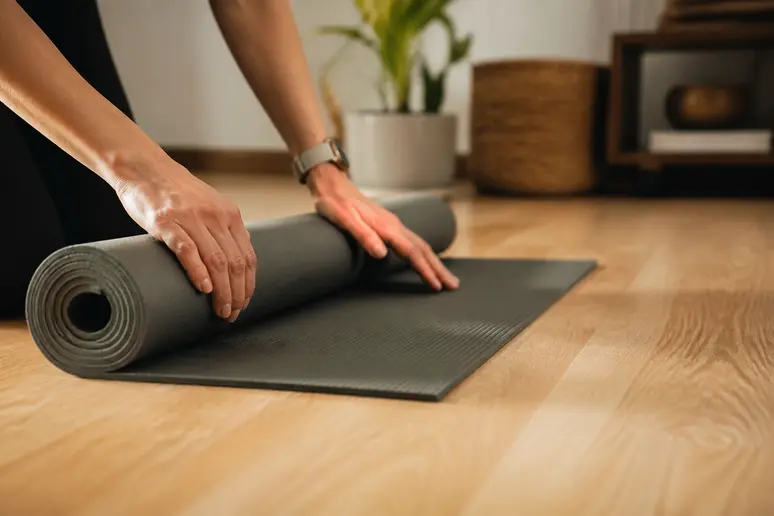 Mains posant un tapis de yoga, préparation pour 7 exercices pour dire adieu au mal de dos