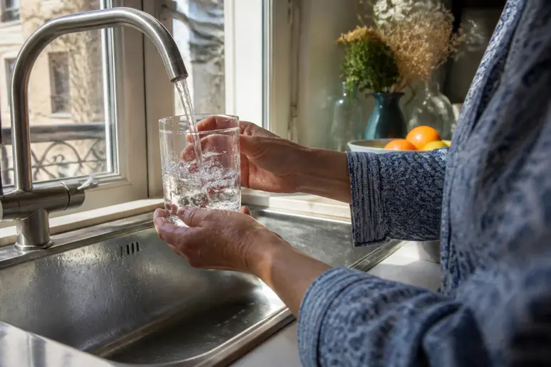 Mains féminines rinçant un verre d'eau, geste préventif contre le caséum.